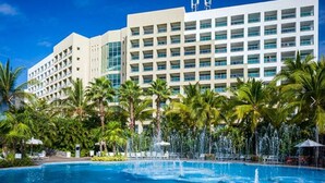 Ett hotell med en stor pool, palmer och en modern byggnadsfasad.