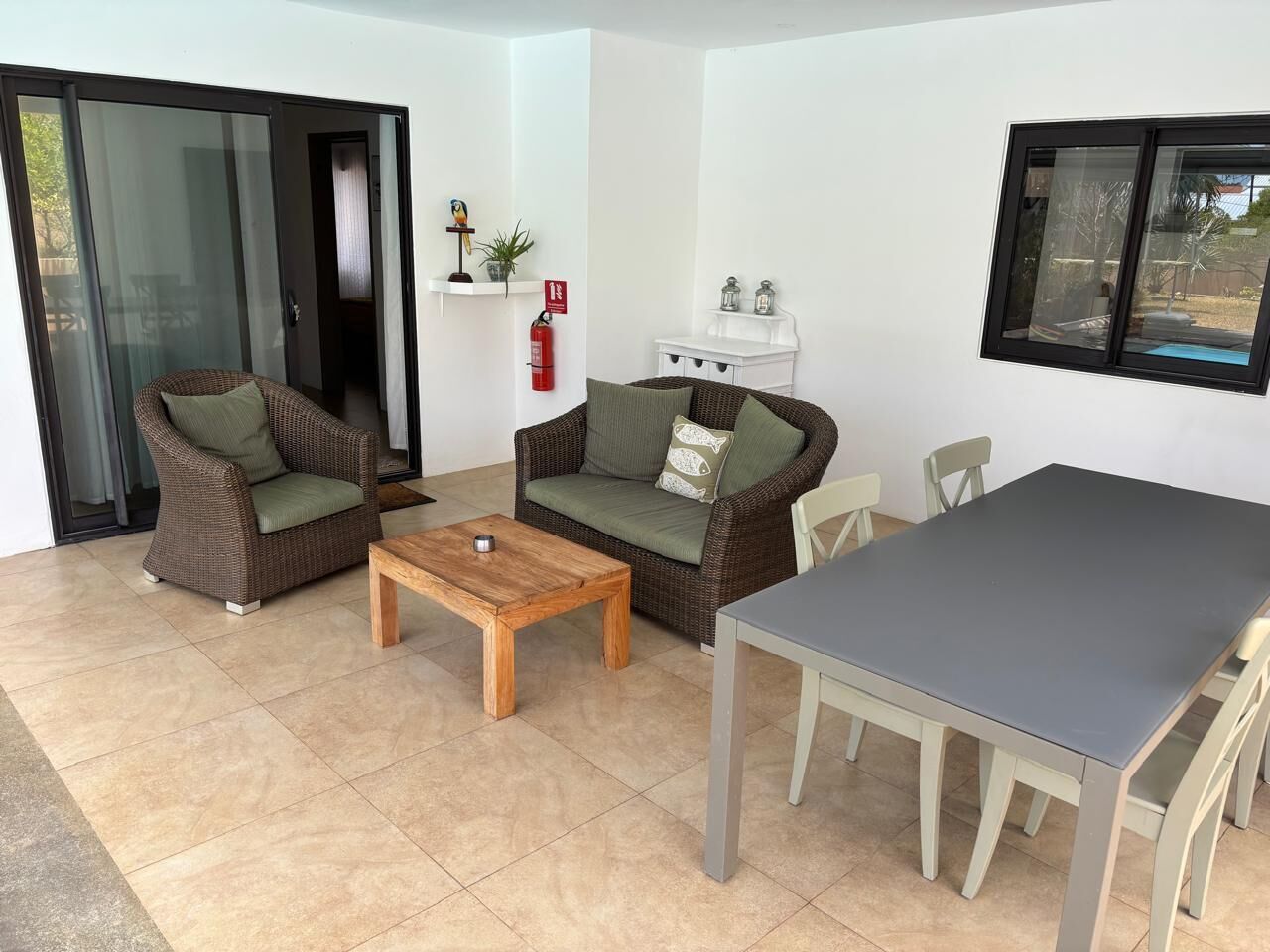 Un salon comprenant deux canapés en osier, une table basse en bois, une table à manger et une porte-fenêtre coulissante donnant sur un espace extérieur.