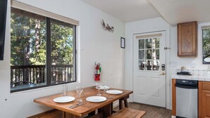 Una cocina compacta con una mesa de madera preparada para comer, una puerta blanca y vistas a árboles a través de una ventana.