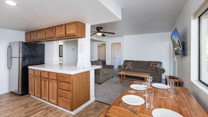 Una cocina moderna con armarios de madera, una isla central y un comedor con una mesa de madera dispuesta para cuatro personas.