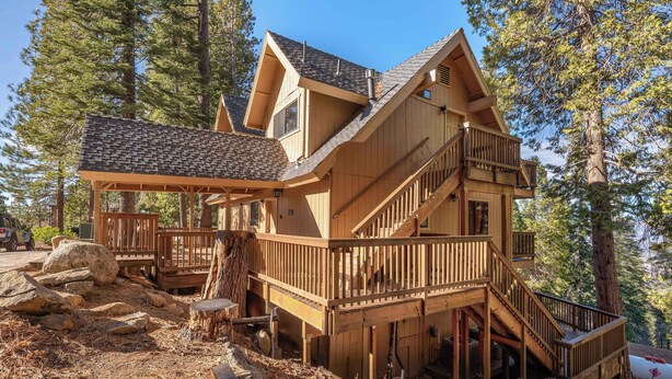 Una cabaña de madera de varios pisos con balcón, escaleras y terraza.