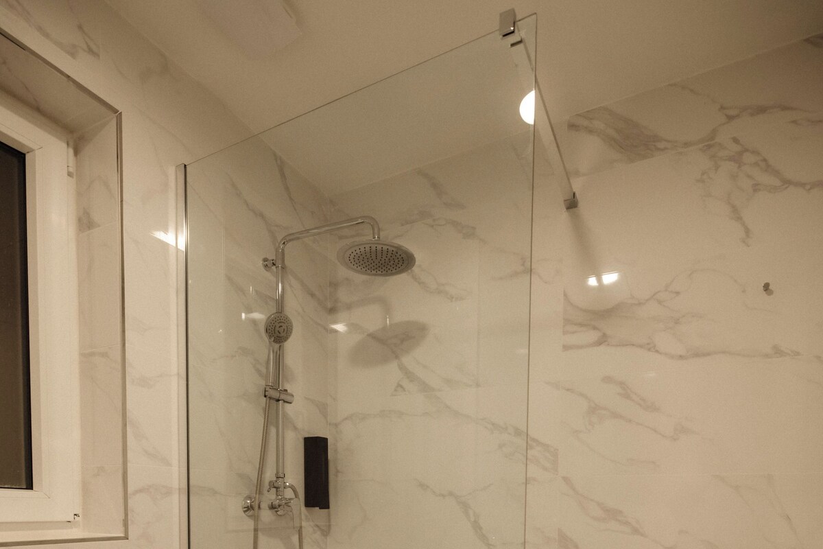 Une salle de bain moderne avec une douche à parois de verre, des toilettes et un sol carrelé en marbre.