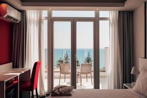 Habitación de hotel con cama, escritorio, silla y vistas al mar a través de amplios ventanales.