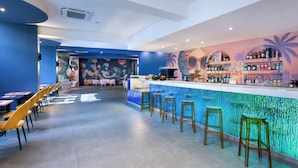 Un espace bar avec un comptoir, des tabourets et une fresque murale représentant des palmiers et des lunettes de soleil.