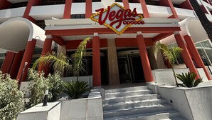 Un immeuble à plusieurs étages, sur lequel on peut voir un grand panneau indiquant un complexe hôtelier de Las Vegas, avec une architecture moderne aux couleurs rouge et blanche, et un escalier menant à l’entrée.