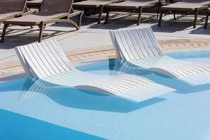 Un área de piscina con sillones de descanso y una piscina azul cristalina.