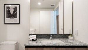 A modern bathroom with a granite countertop, a white sink, and a framed picture of Los Angeles on the wall.