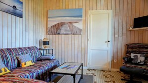 A room with a striped wall, a sofa with colorful cushions, a small table, a chair, and a door.