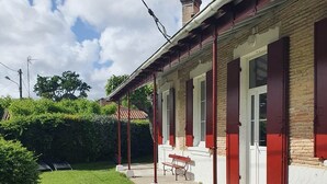 A building with a brick facade, red shutters, and a covered porch with a bench.