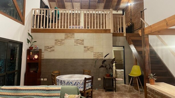 Une pièce chaleureuse avec un plafond en bois, un balcon, un coin repas avec une table et des chaises, et un escalier.