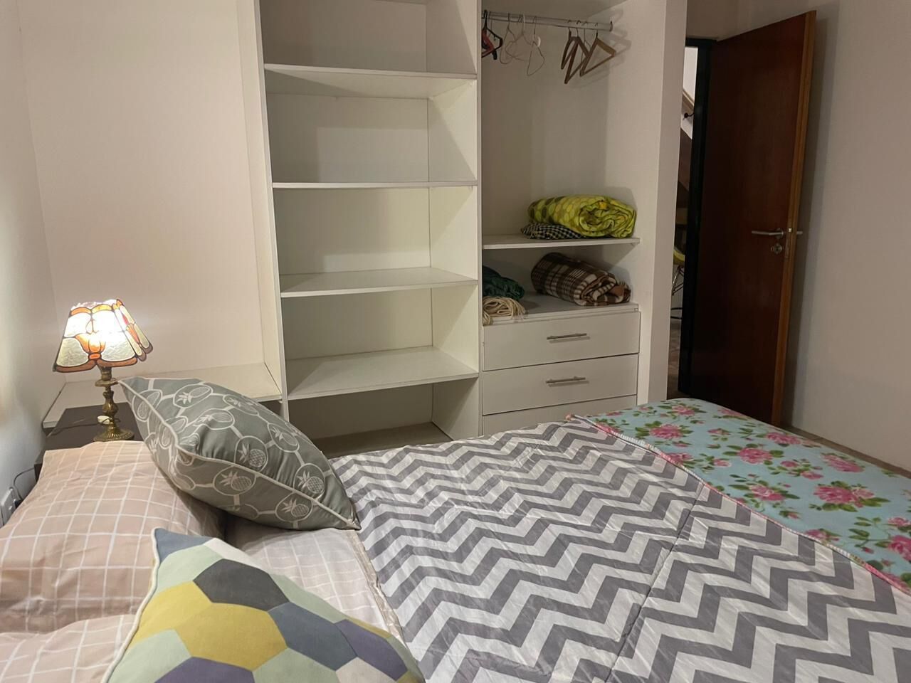 Makuuhuone, jossa on sänky, yöpöytä lampun kanssa, vaatekaappi ja ovi.
