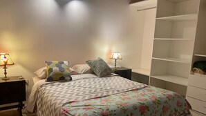 Une chambre à coucher avec un lit, deux tables de chevet avec des lampes, une armoire blanche et une couvre-lit à motifs floraux.
