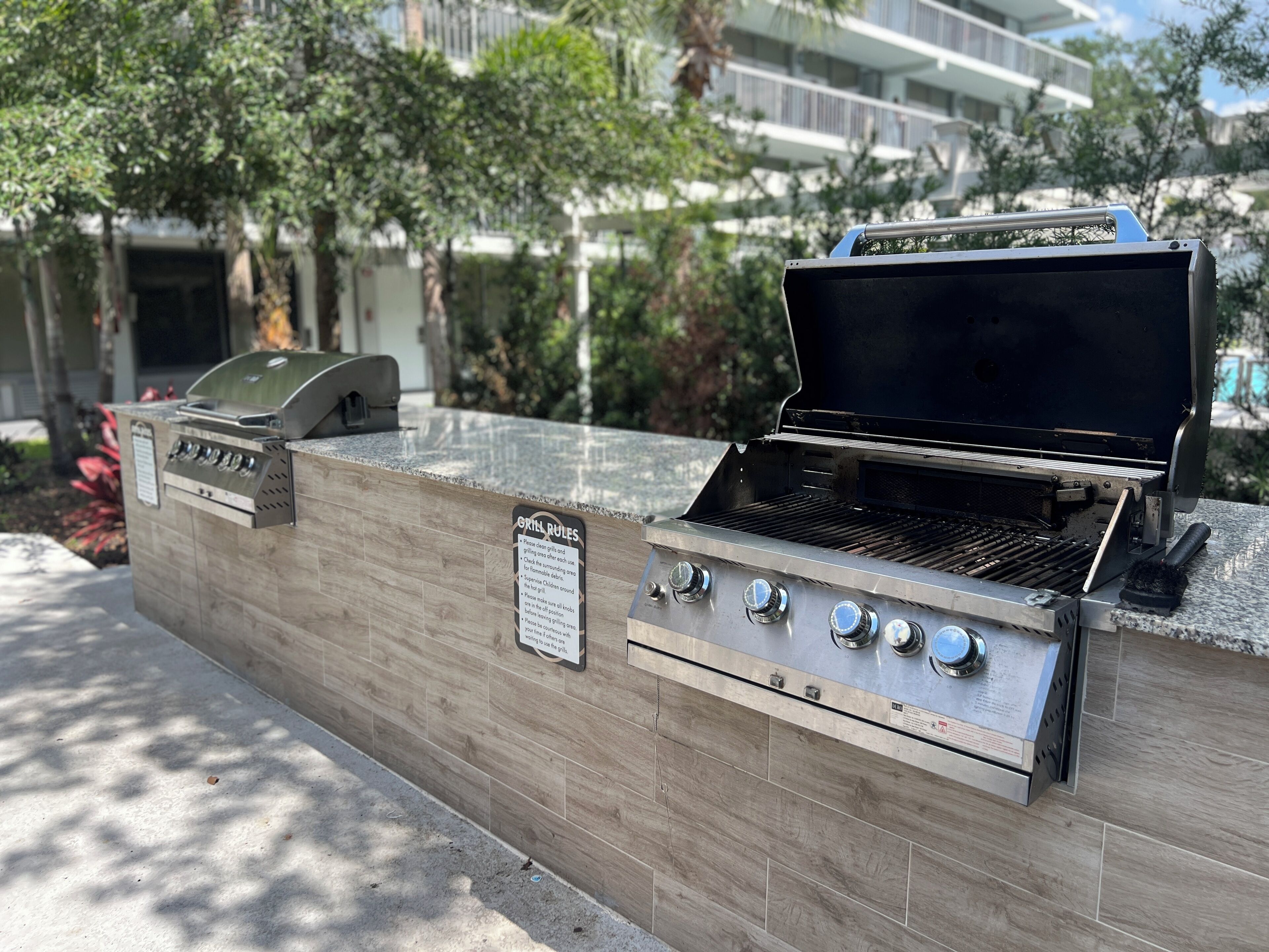 An outdoor grill station with a grill rules sign, a gas grill, and a charcoal grill.