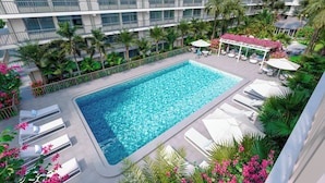 Un hôtel doté d’une grande piscine entourée de chaises longues et de palmiers.