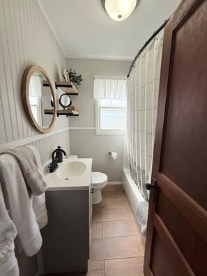 A bathroom with a white sink, a toilet, a mirror, and a shower area.