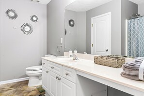 A bathroom with a white toilet, a sink with a mirror above it, and decorative wall art. - Beautiful 3bd/2ba peaceful home in Lawrenceville with Gym, Office, and Jacuzzi (Lawrenceville)