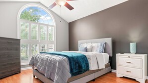 Un dormitorio con cama, mesita de noche, cómoda y ventana con persianas.