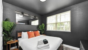 Ein modernes Hotelzimmer mit einem großen Bett, zwei Nachttischen, einem kleinen Tisch und einem großen Fenster.