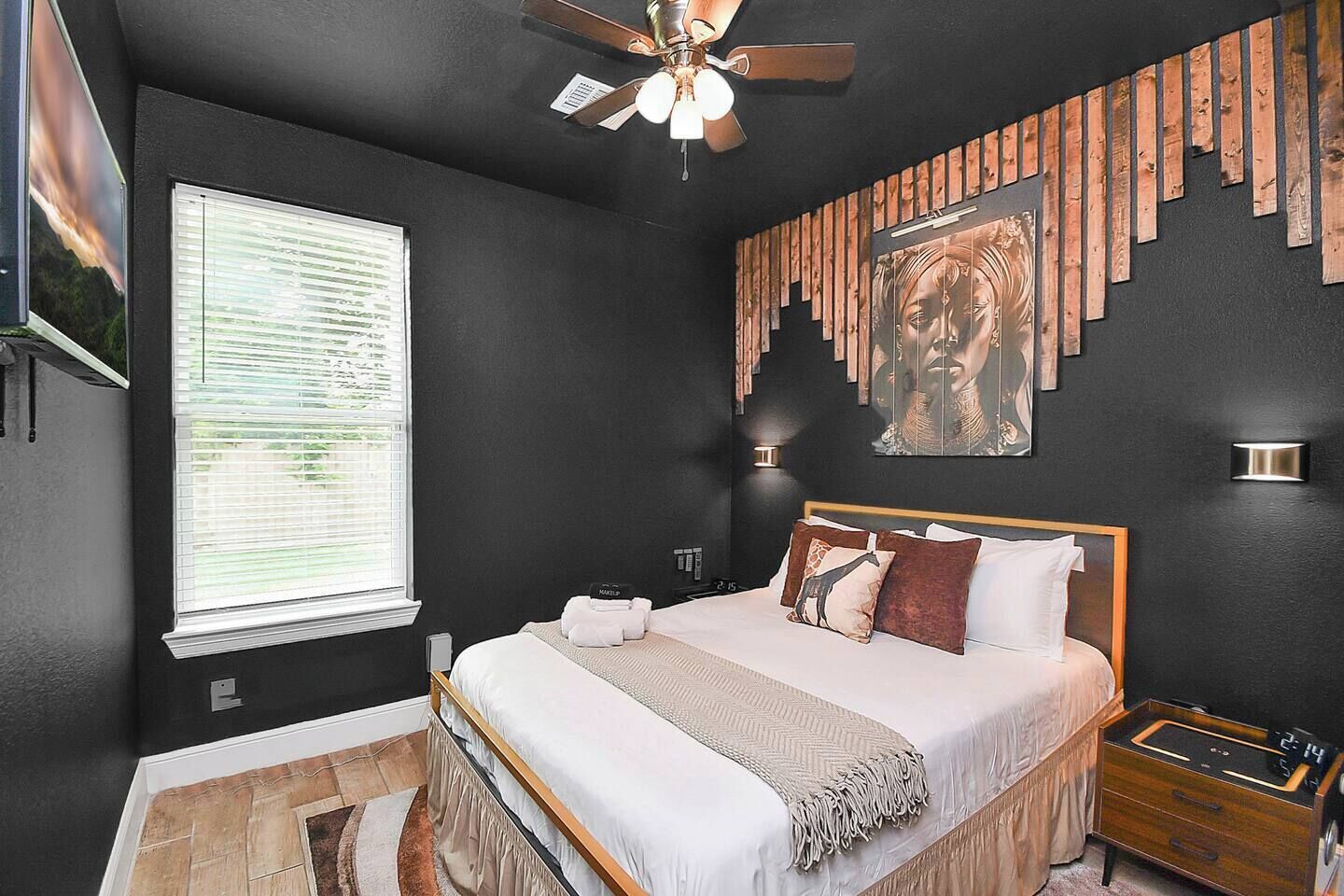 Een moderne slaapkamer met een groot bed, een plafondventilator, een houten hoofdbord en een wanddecoratie.