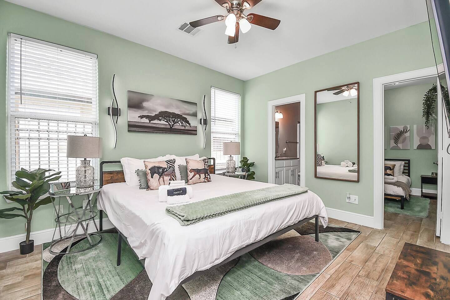 A bedroom with a bed, bedside tables, a ceiling fan, a large mirror, and artwork on the walls.