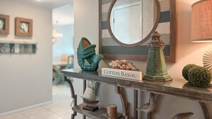 A hallway with a glass console table displaying decorative items, a mirror, and a sign reading "Cotton Bayou".