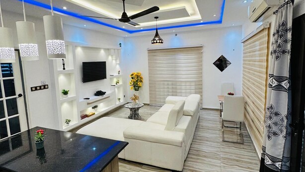 A modern living room with a sofa, a coffee table, and a TV. There is a ceiling fan and pendant lights. - Magnificent T3 near the airport (Cotonou)