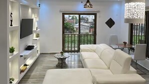 A modern living room with a white sofa, a TV mounted on the wall, and a ceiling fan. - Magnificent T3 near the airport (Cotonou)