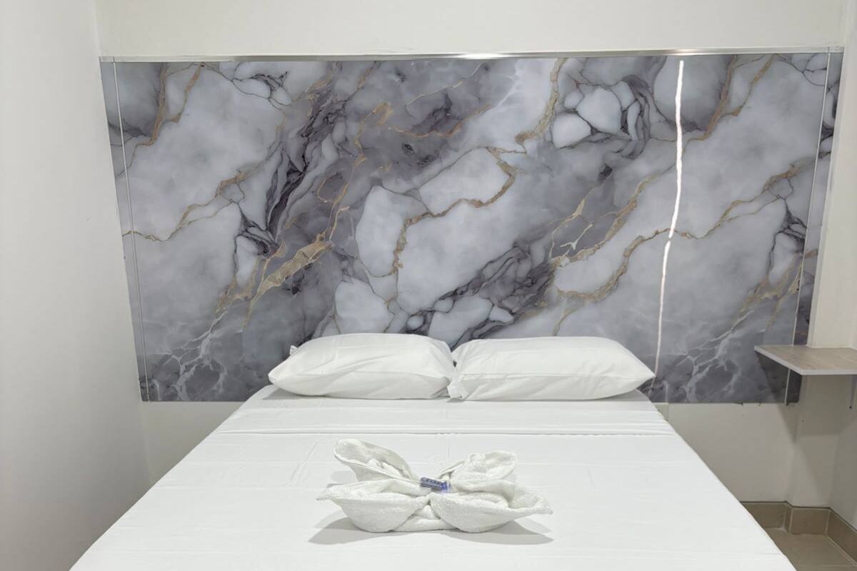 A bed with a marble-patterned headboard, white bedding, and a towel on the bed.