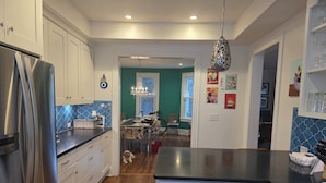 A modern kitchen with stainless steel appliances, a dining area with patterned chairs, and a hallway leading to another room. - 3-bedroom house in charming College Hill, Easton, PA with WiFi, AC. Book now (Easton)