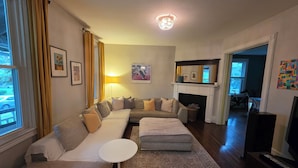 A living room with a sectional sofa, a small round table, a fireplace, and a television. - 3-bedroom house in charming College Hill, Easton, PA with WiFi, AC. Book now (Easton)