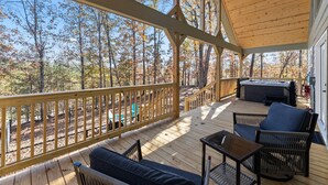 Una terraza techada con mobiliario exterior, un jacuzzi y vistas a un bosque.