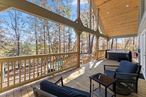 Una terraza techada con mobiliario exterior, un jacuzzi y vistas a un bosque.