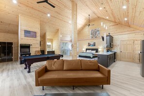 A spacious room with a pool table, a sofa, a ceiling fan, and wooden walls.