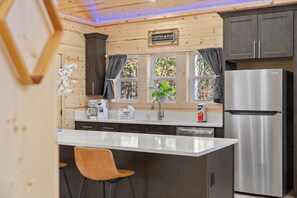 A kitchen with wooden walls, a stainless steel refrigerator, a coffee bar sign, and a window with curtains.