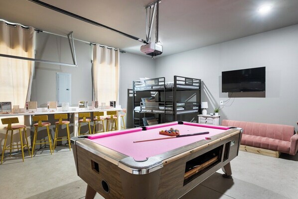 A room with a pool table, bunk beds, a bar area, and a television.