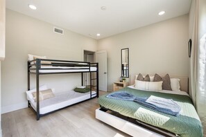 A bedroom with bunk beds, a single bed, a bedside table, a mirror, and a window with curtains.