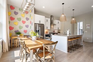 A modern kitchen with white cabinets, a stainless steel refrigerator, and a wooden dining table with four chairs.
