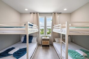 A room with bunk beds, a small table with a plant, and a window with curtains.