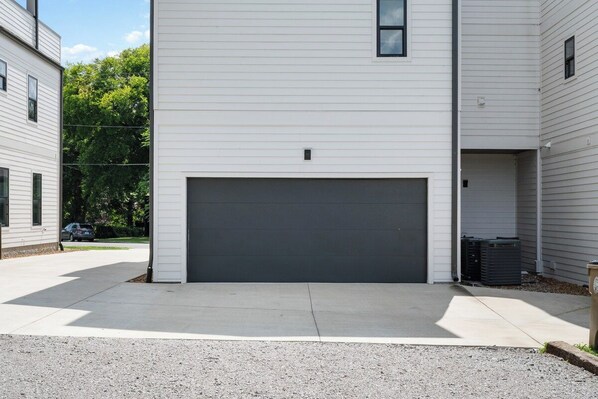 A two-story residential building with a dark-colored garage door, a small window on the upper floor, and a visible air conditioning unit on the ground floor.