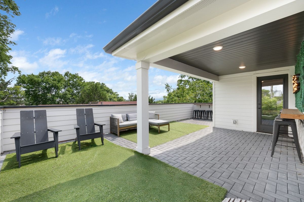 An outdoor patio with a covered seating area, artificial grass, and a brick floor.
