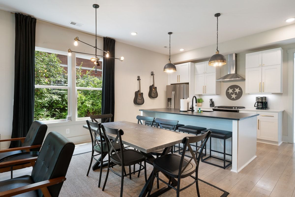 A modern kitchen with a central island, bar stools, and a dining area with a table and chairs.