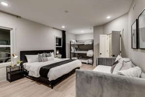 A modern bedroom with a large bed, bedside tables, a bunk bed, a seating area, and a wardrobe.