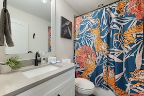 A bathroom with a white sink, a mirror, a towel rack, a toilet, and a shower curtain with a tiger and floral pattern.