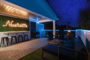 An outdoor patio with a seating area, a bar counter, and a wall with illuminated letters.