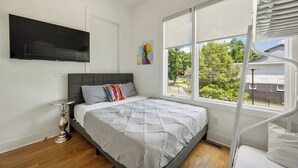 A bedroom with a bed, a TV mounted on the wall, a window with a view of trees, and a spiral staircase. - 16 Bed Private Gulch Home with Rooftop (Nashville)