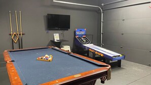 A pool table with balls and cues, a television mounted on the wall, and a hot shot arcade machine. - 16 Bed Private Gulch Home with Rooftop (Nashville)