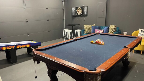 A pool table with a cue stick, a dartboard, and a sofa with cushions. - 16 Bed Private Gulch Home with Rooftop (Nashville)