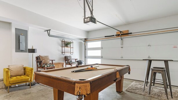 A pool table in a room with a garage door, a yellow armchair, and a ceiling-mounted projector. - 19 Bed Home Near Downtown with Game room (Nashville)
