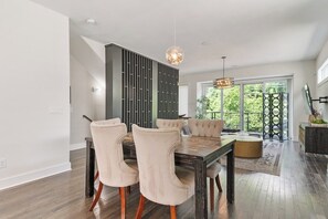 Un coin repas avec une table en bois foncé, des chaises recouvertes d’un tissu beige et un luminaire suspendu moderne.