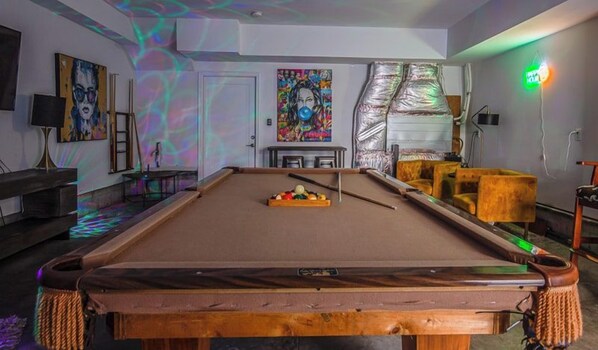 A pool table in a room with a door, artwork on the walls, and a neon sign.